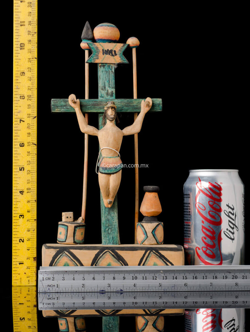 Hand Carved Wooden Cross on a platform with elements of the passion such as a spear, a sponge (used to give him vinegar) and the dice. The cross is painted in green and the decor is very simple, naive style with a christ with smiling expression.  Rulers