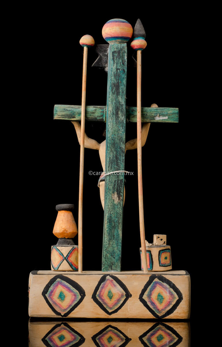 Hand Carved Wooden Cross on a platform with elements of the passion such as a spear, a sponge (used to give him vinegar) and the dice. The cross is painted in green and the decor is very simple, naive style with a christ with smiling expression. Back