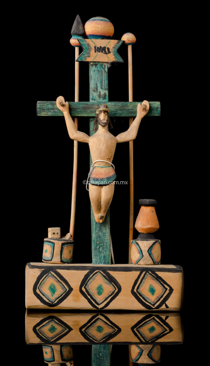 Hand Carved Wooden Cross on a platform with elements of the passion such as a spear, a sponge (used to give him vinegar) and the dice. The cross is painted in green and the decor is very simple, naive style with a christ with smiling expression. 