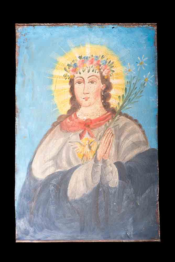 Mexican Retablo el alma de maria with virgin mary holding a branch between her hands in prayer position near hear heart. At the center of her chest is an image of the holly spirit. Her head is adorned by a crown of flowers. Her dress is blue and white and the background is light blue
